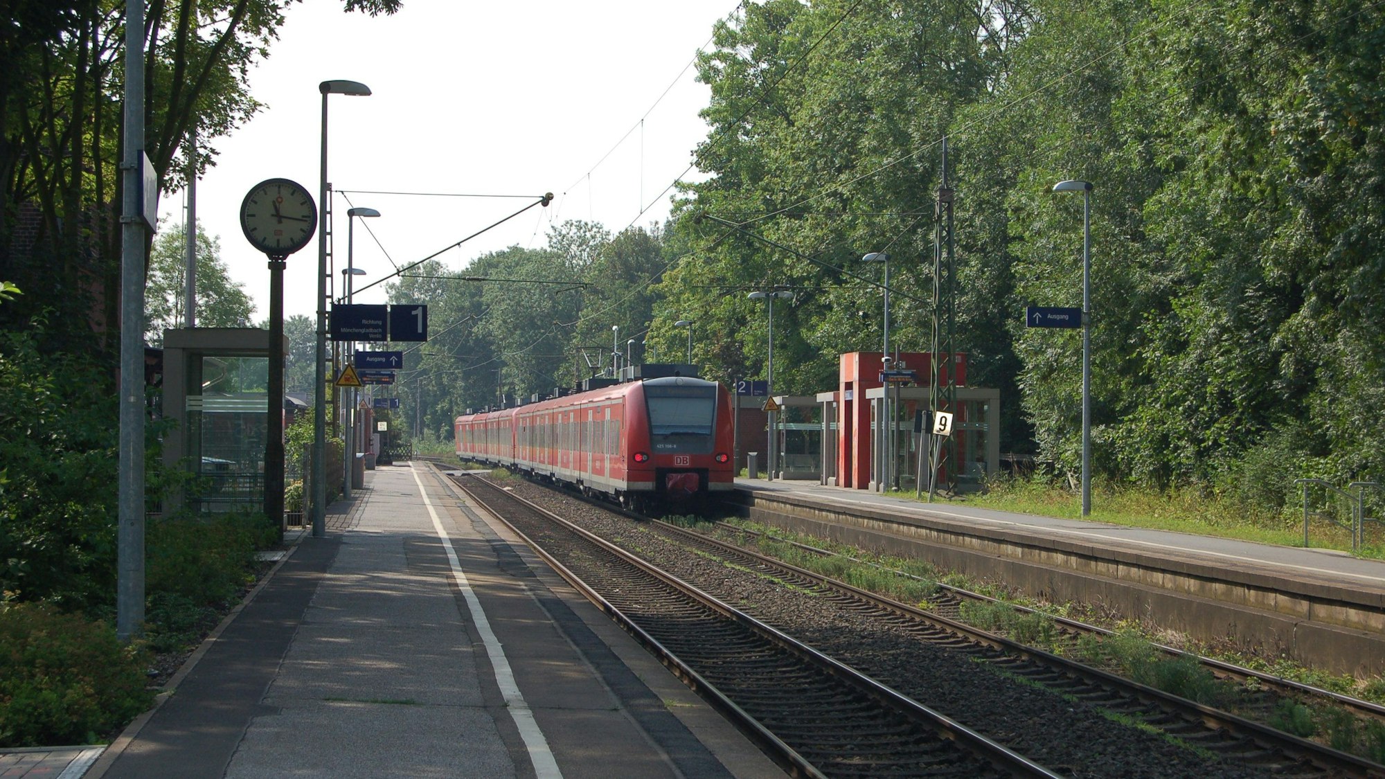Zu sehen ist ein Bahnhof, in den gerade ein roter Zug einfährt.