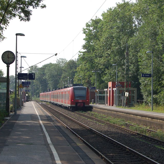 Zu sehen ist ein Bahnhof, in den gerade ein roter Zug einfährt.&nbsp;