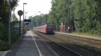 Zu sehen ist ein Bahnhof, in den gerade ein roter Zug einfährt.&nbsp;
