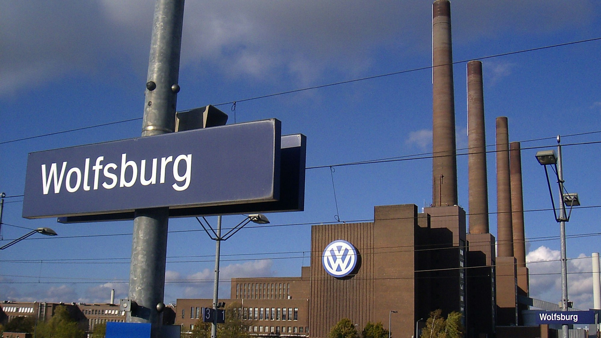 Blick von einem Bahnsteig des Wolfsburger Hauptbahnhofs auf das Volkswagen-Werk mit seinen charakteristischen Schornsteinen.