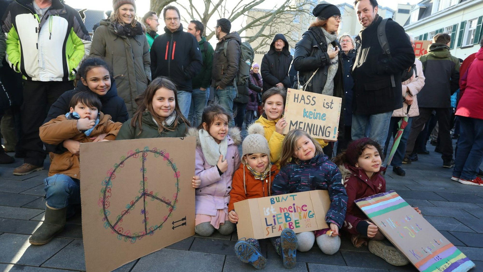 Kinder hocken mit Plakaten, die beispielsweise das Friedenszeichen zeigen, auf dem Marktplatz.