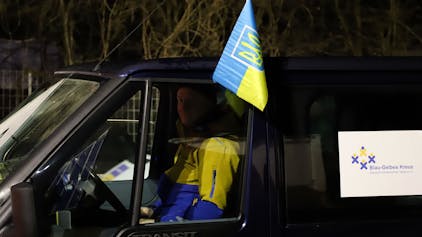 Ein Mann in blau-gelber Jacke sitzt in einem Transporter mit der Aufschrift „Blau-Gelbes Kreuz“ und einer Ukraineflagge.