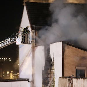 Feuerwehrleute löschen von einer Drehleiter aus ein brennendes Gebäude. Es dringt dichter Rauch aus dem Haus