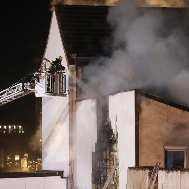 Feuerwehrleute löschen von einer Drehleiter aus ein brennendes Gebäude. Es dringt dichter Rauch aus dem Haus