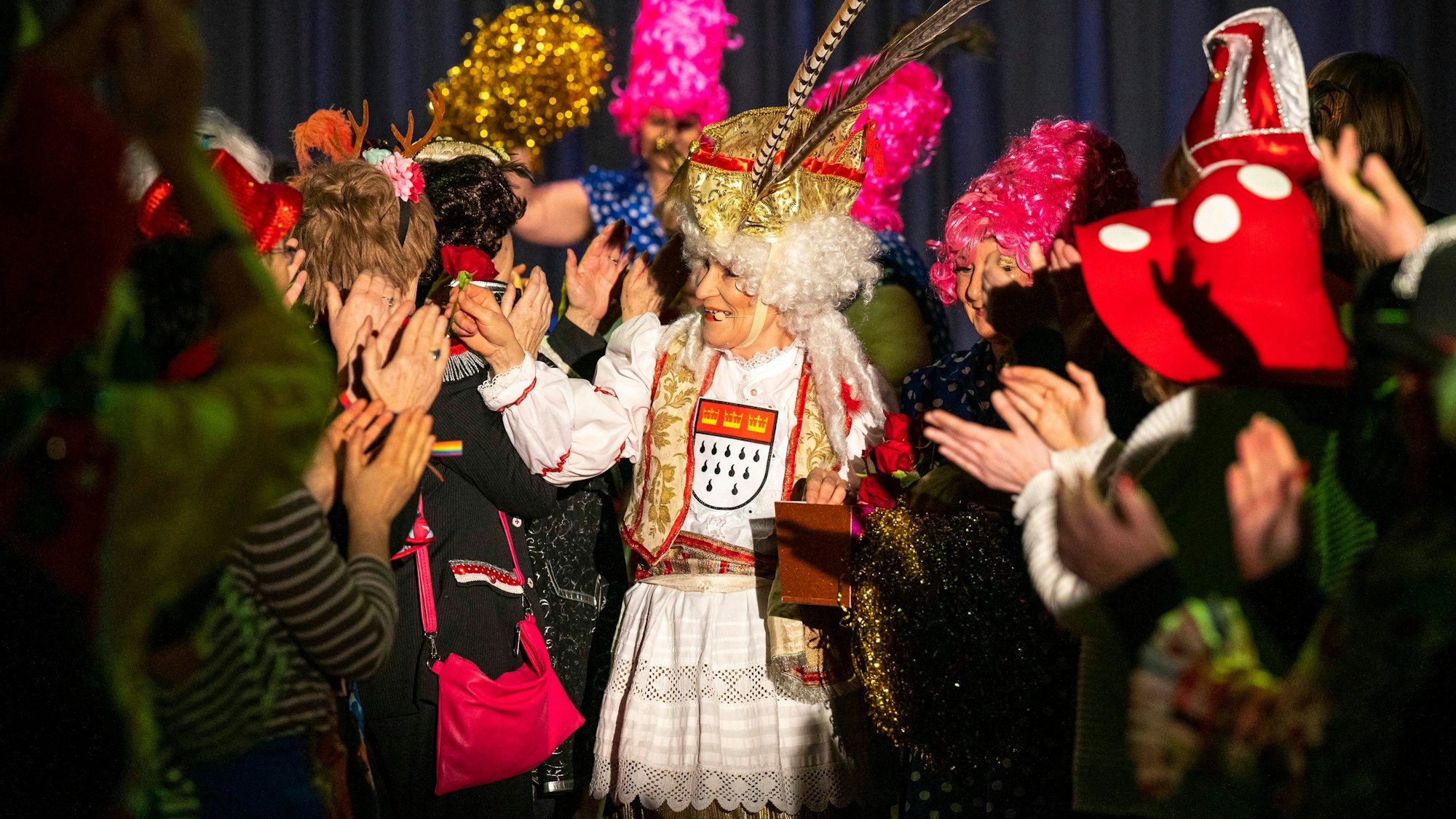 Eine als Prinz Karneval verkleidete Schauspielerin geht durch die Reihen des Publikums.