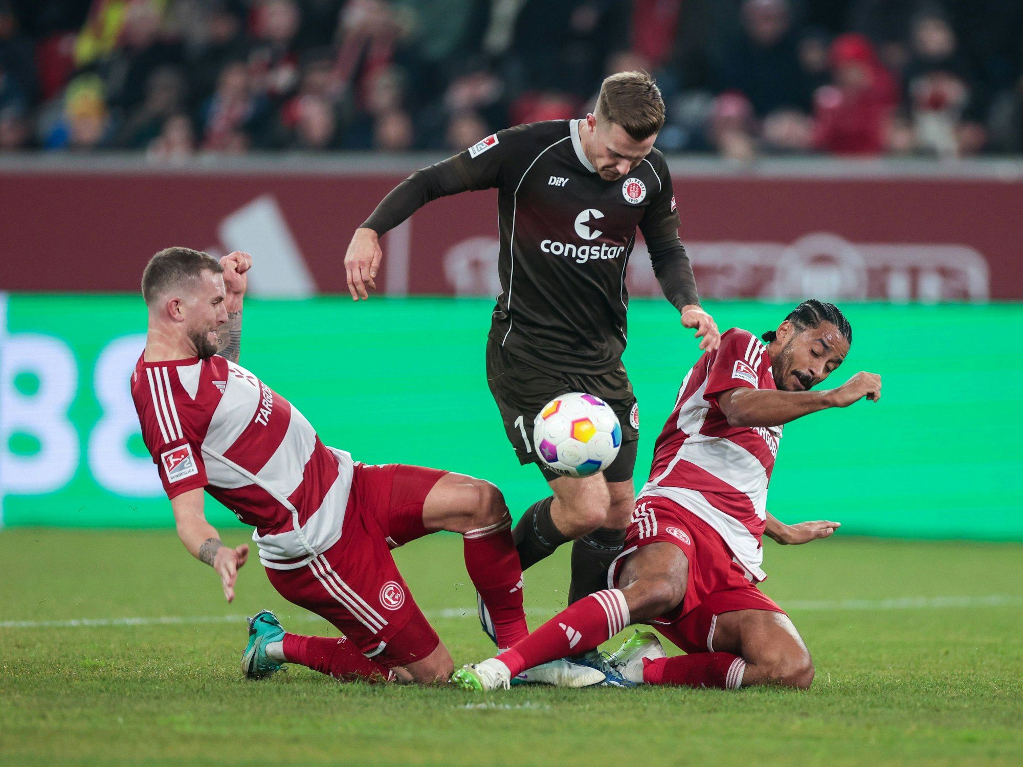 Fortuna Düsseldorfs Kapitän Andre Hoffmann (l.) und Teamkollege Emmanuel Iyoha (r.) grätschen gegen St. Paulis Johannes Eggestein.