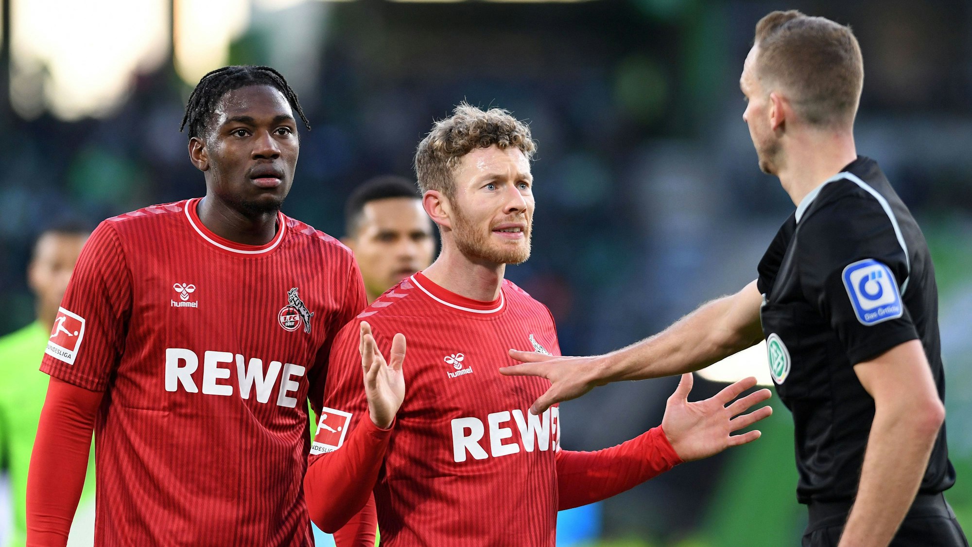Faride Alidou, Florian Kainz (beide 1. FC Köln) diskutieren in Wolfsburg mit Schiedsrichter Sören Storks.