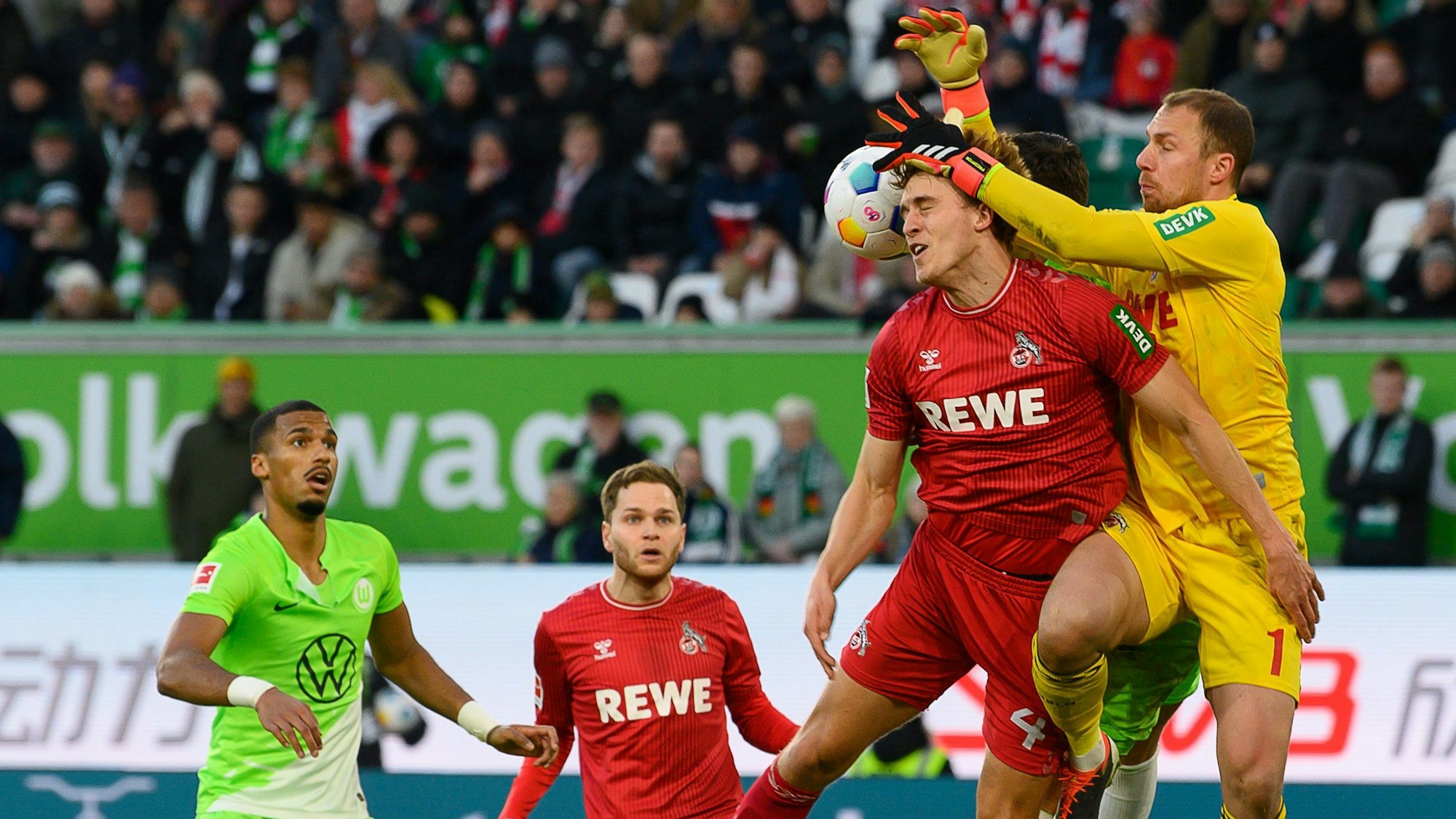 Kölns Torwart Marvin Schwäbe (r) und Kölns Timo Hübers kämpfen mit Wolfsburgs Jonas Wind (verdeckt) um den Ball.