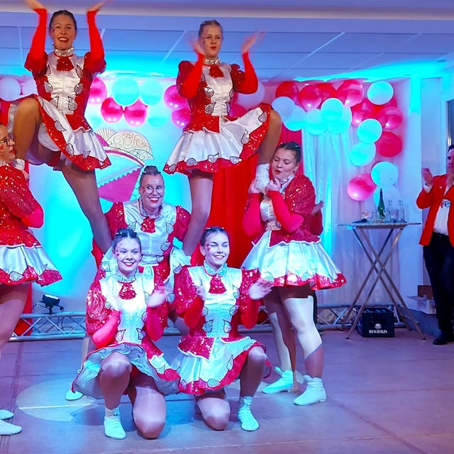 Sieben junge Frauen der Tanzgarde zeigen eine Akrobatische Pose auf einer Bühne.
