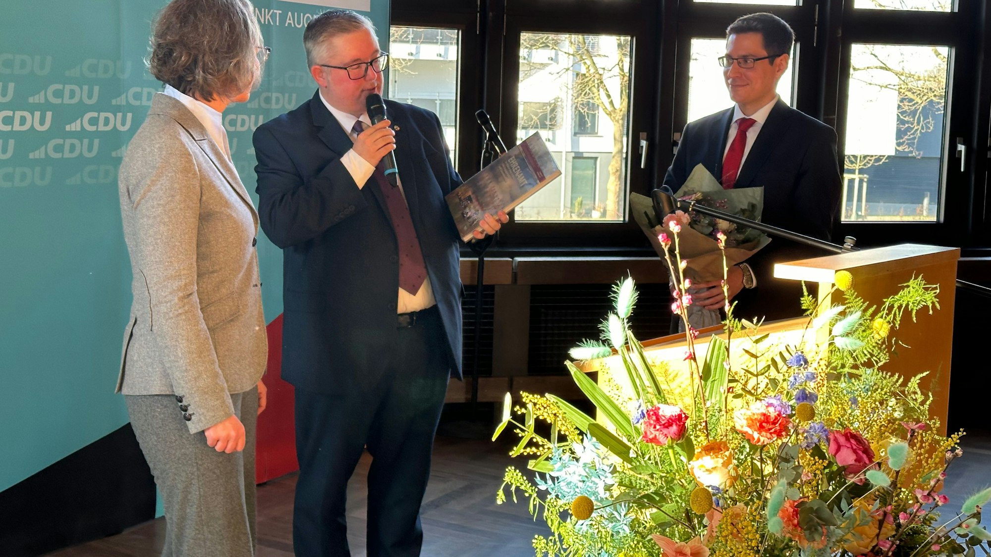 NRW-Ministerin Ina Scharrenbach bekam von Sascha Lienesch und Bürgermeister  Max Leitterstorf das Jahresheft des Kreises geschenkt. Im Vordergrund des Bildes ein bunter Blumenstrauß.