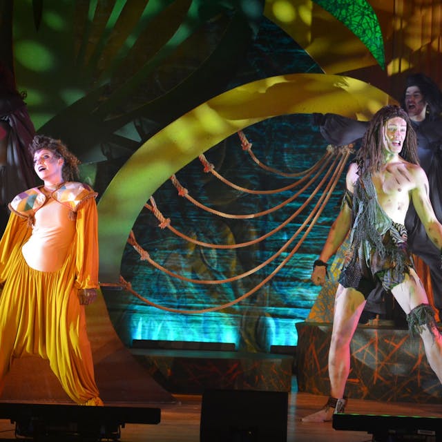 Das Bild zeigt zwei als Tarzan und Tee verkleidete Schauspieler auf einer bunt dekorierten Bühne.