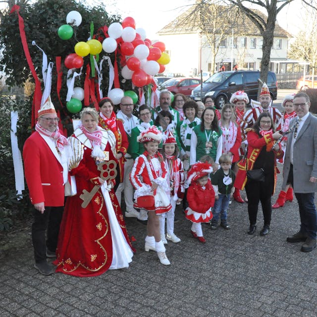 Vertreter und Vertreterinnen der Karnevalsgesellschaften und -vereine der Gemeinde Nettersheim stehen vor einem mit Luftballons und Krepppapier geschmücktem Busch am Rathaus in Zingsheim.