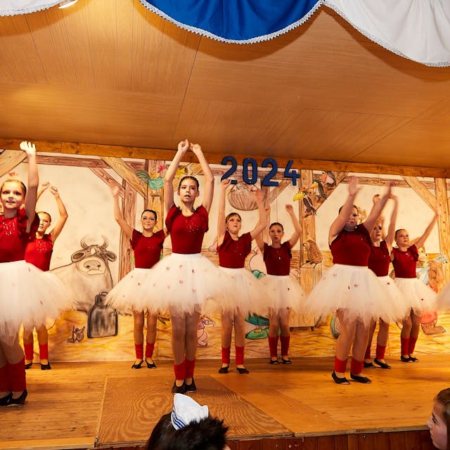Eine Gruppe junger Mädchen tanzt in weißen Tüll-Röcken und roten T-Shirts auf einer Bühne.