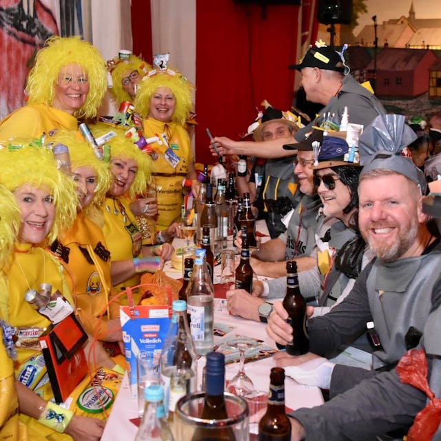 Besucher einer Karnevalssitzung: Links sitzen Frauen in gelben Kostümen, die Wertstoffbeutel darstellen, rechts Männer in grauen Kostümen als Beistellsack zur Restmülltonne.