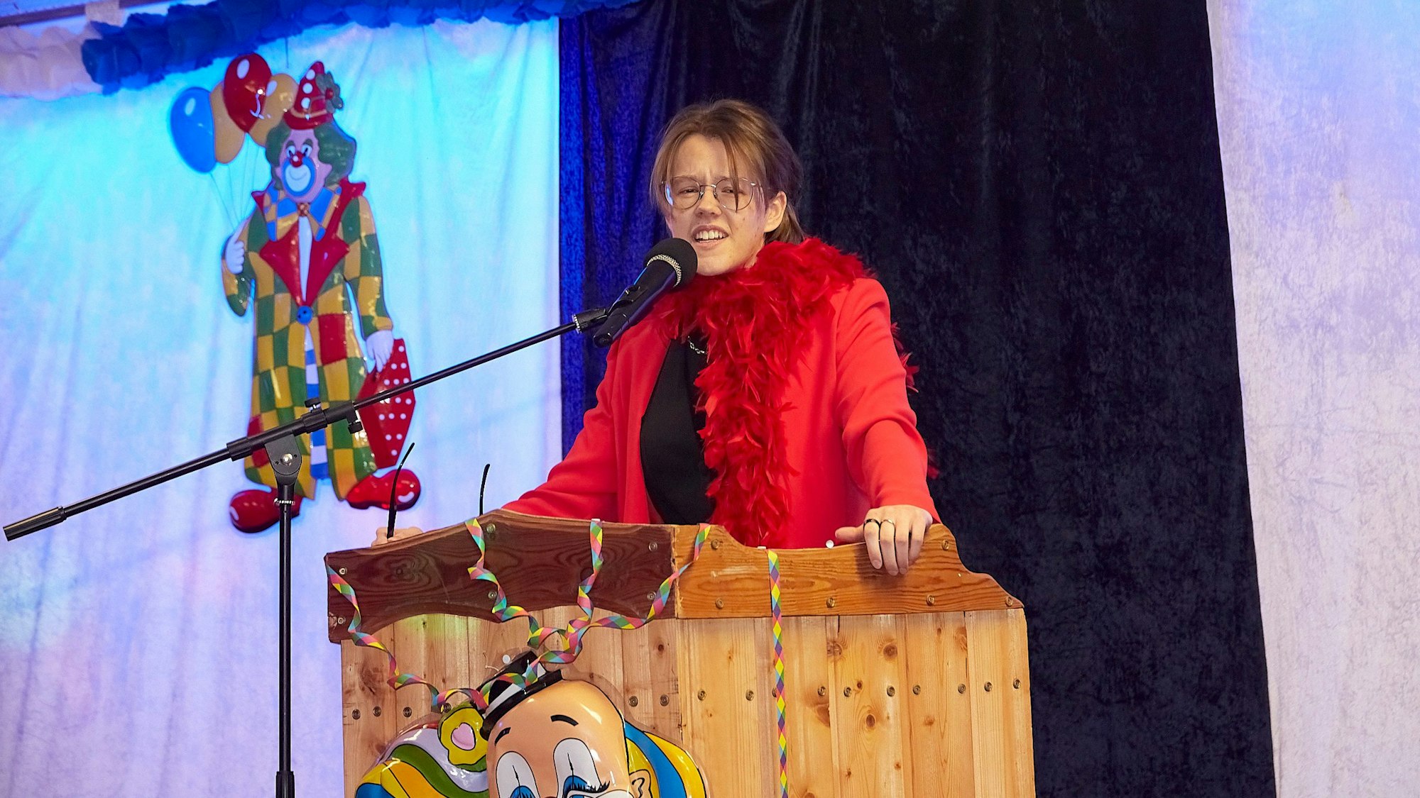 Denise Wiesen trägt ein Kostüm mit roter Federboa und steht in der Karnevalsbütt in Wahlen.