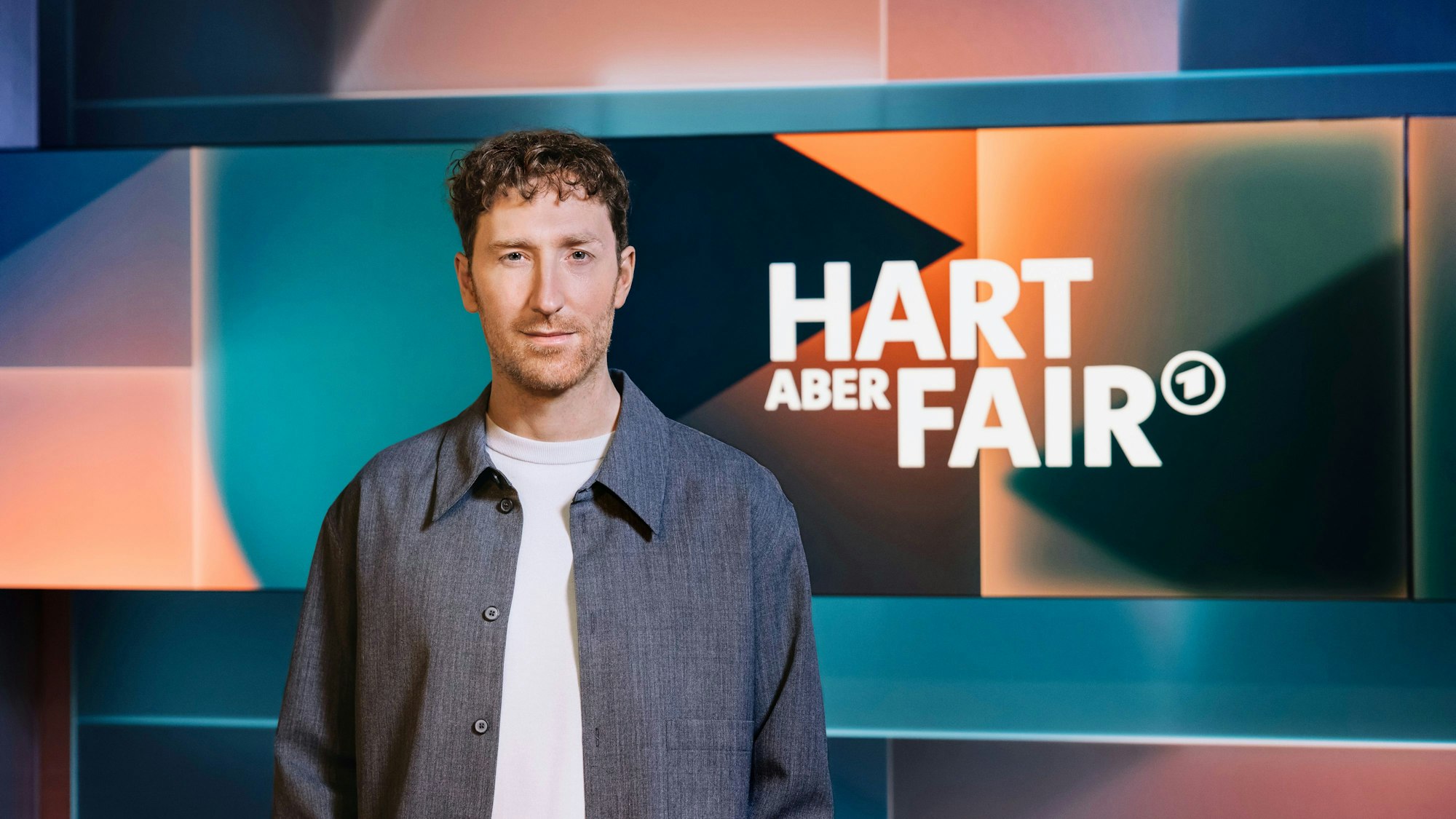 Moderator Louis Klamroth steht vor dem Logo der ARD-Talkshow „Hart aber fair“ in einem Fernsehstudio. Das Aussehen und die inhaltliche Ausrichtung des Formats ändern sich ab Januar 2024.