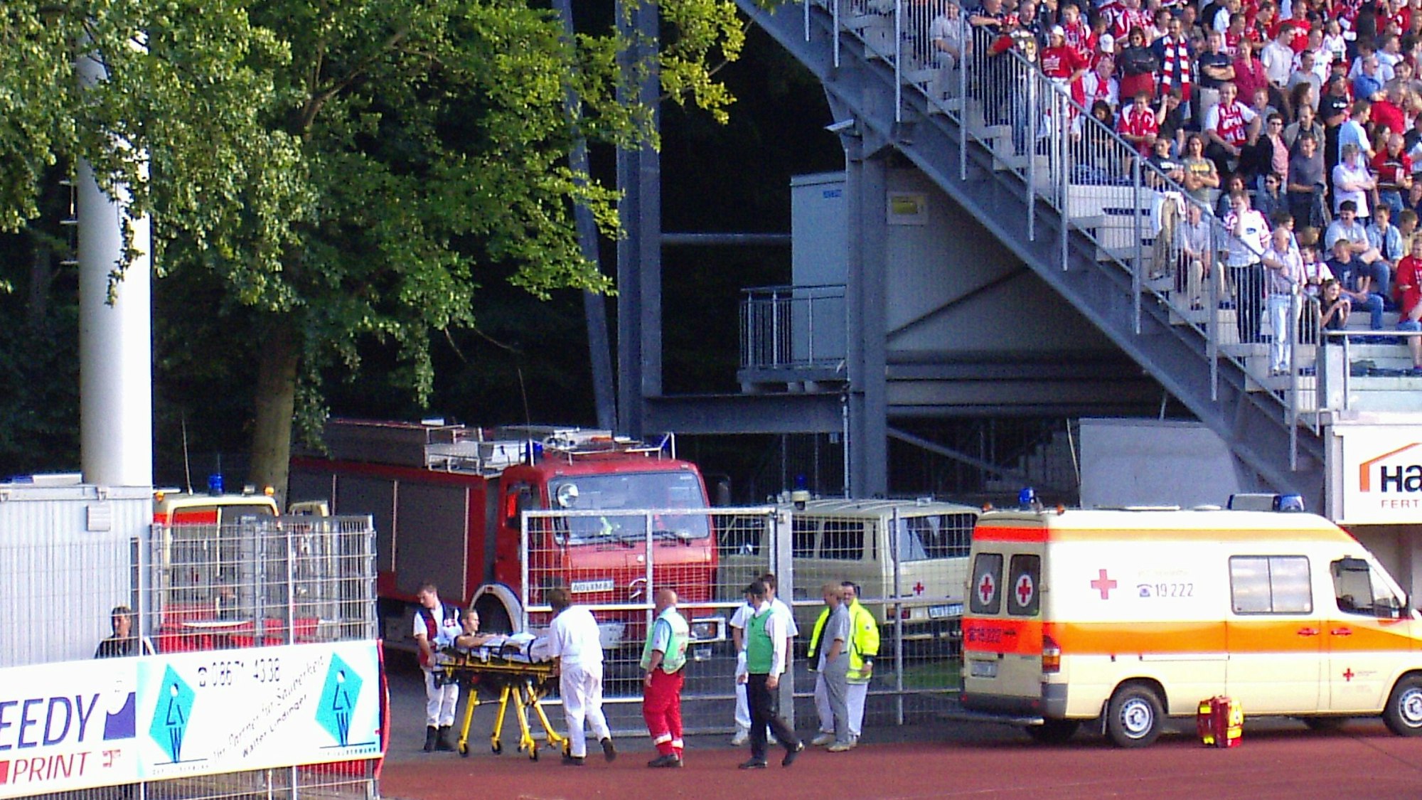 Eine Person wird auf einer Krankentrage aus einem Fußballstadion gefahren. Mehrere Sanitäter begleiten ihn.
