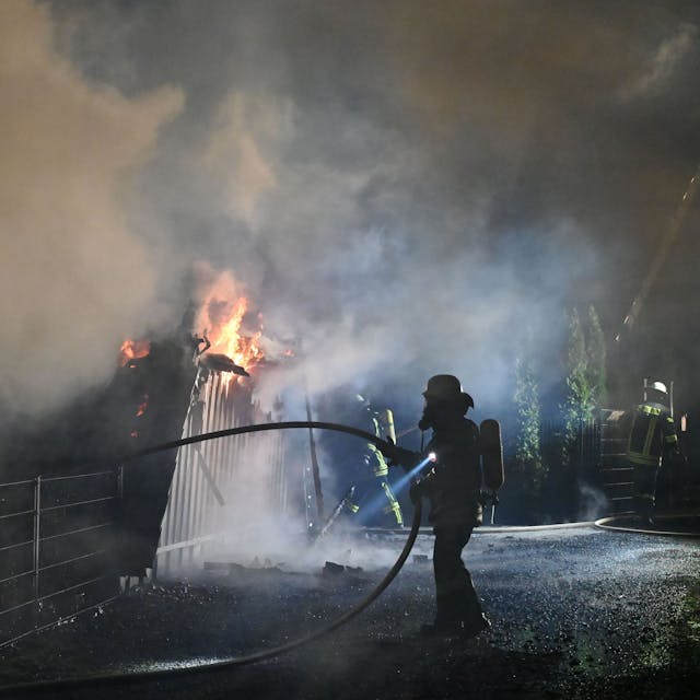 Feuerwehrleute mit Atemschutzausrüstung sind an den brennenden Überresten des dreieckigen Ferienhauses in Freilingen zu sehen.