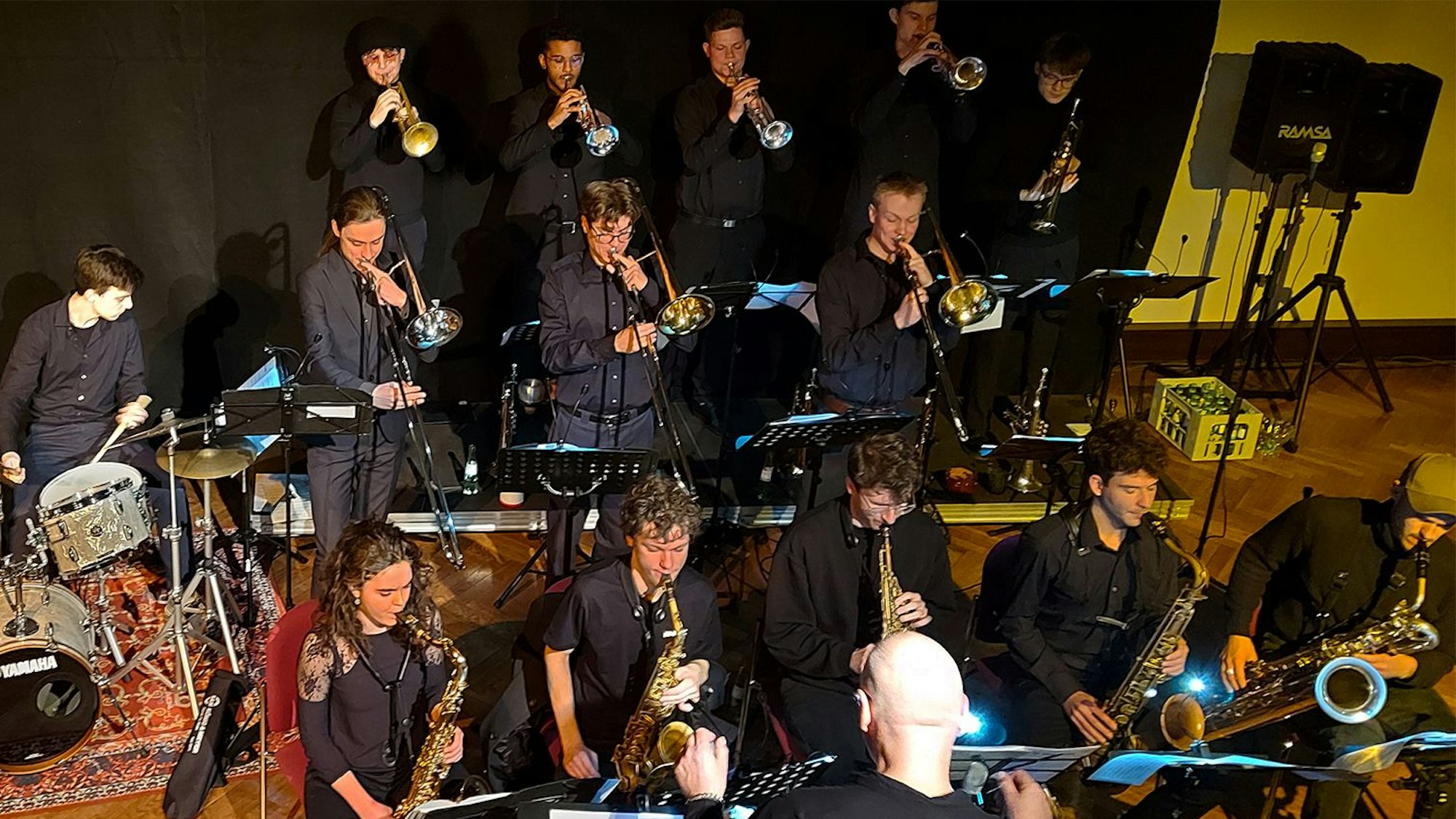 Die Musikerinnen und Musiker stehen und sitzen in der klassischen Big-Band-Aufstellung auf der Bühne, vorne fünf Akteure mit Saxofon.