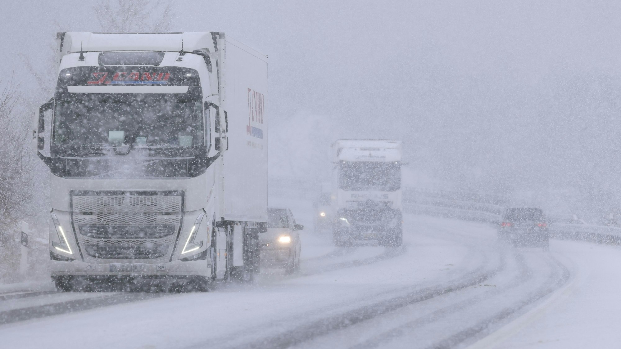 Mehrere Fahrzeuge sind bei starkem Schneefall auf einer Bundesstraße in der Eifel unterwegs. Die Fahrbahn ist zu großen Teilen mit Schnee bedeckt.