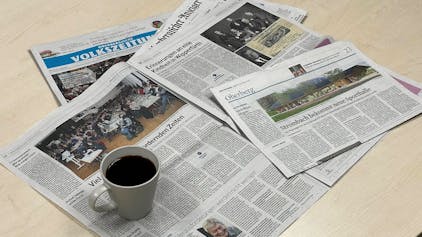 Zeitungsausgaben der Oberbergischen Volkszeitung und des Oberbergischen Anzeigers liegen auf einem Tisch. Darauf steht eine Tasse Kaffee.