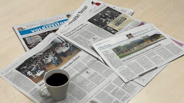 Zeitungsausgaben der Oberbergischen Volkszeitung und des Oberbergischen Anzeigers liegen auf einem Tisch. Darauf steht eine Tasse Kaffee.