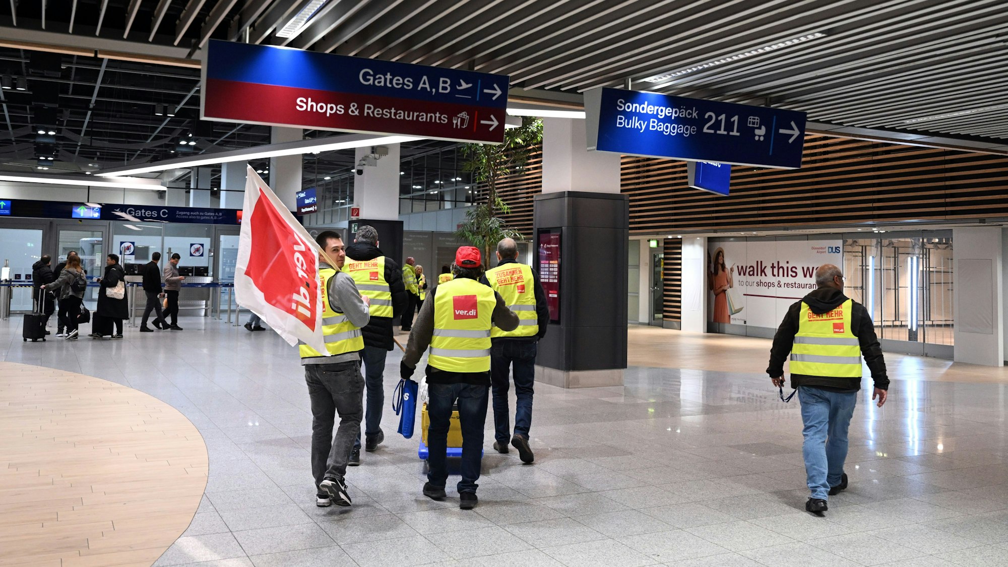 Männer gehen mit einer Verdi-Fahne durch einen Flughafen während eines Streiks.
