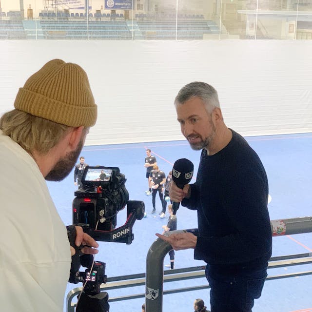 „TV Total“-Moderator Sebastian Pufpaff beim Handballtraining in der Schwalbe-Arena. Er spricht in ein Mikrofon und wird dabei von einem Kameramann gefilmt.