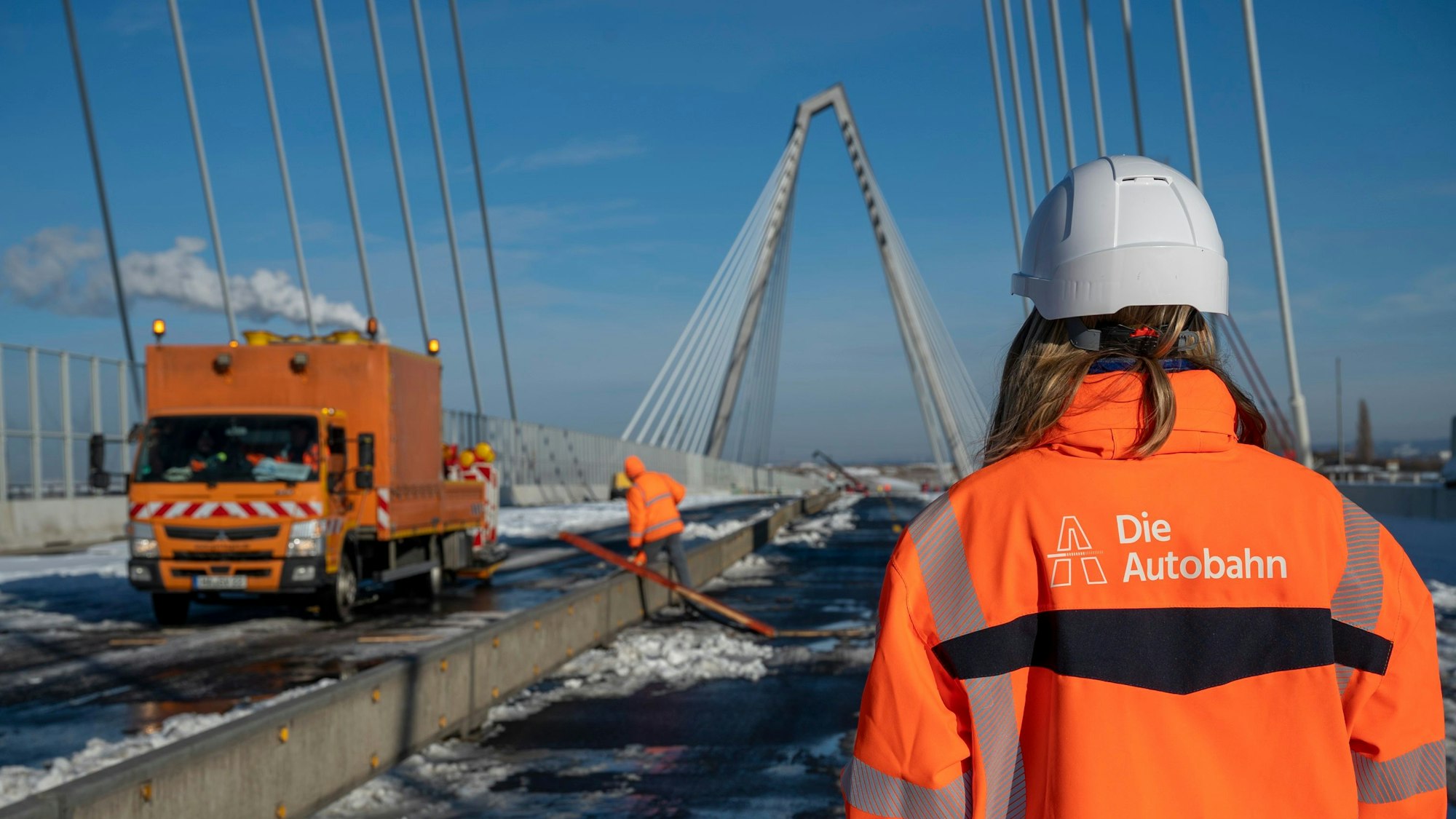 Bauarbeiter in oranger Arbeitskleidung sind auf der Brücke zu sehen, ebenso wie ein Fahrzeug der Autobahn AG.