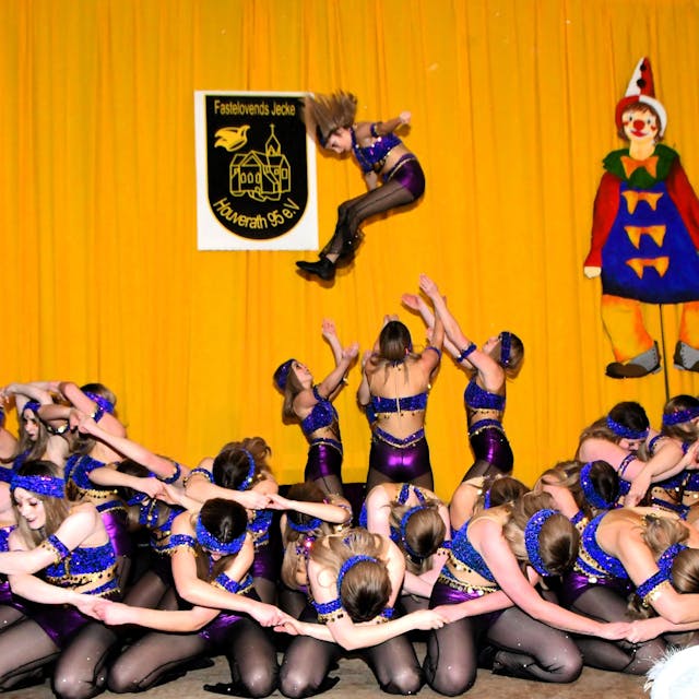 Tänzerinnen knien auf der Bühne, während im Hintergrund ein Mädchen von drei anderen in die Höhe geworfen wird.