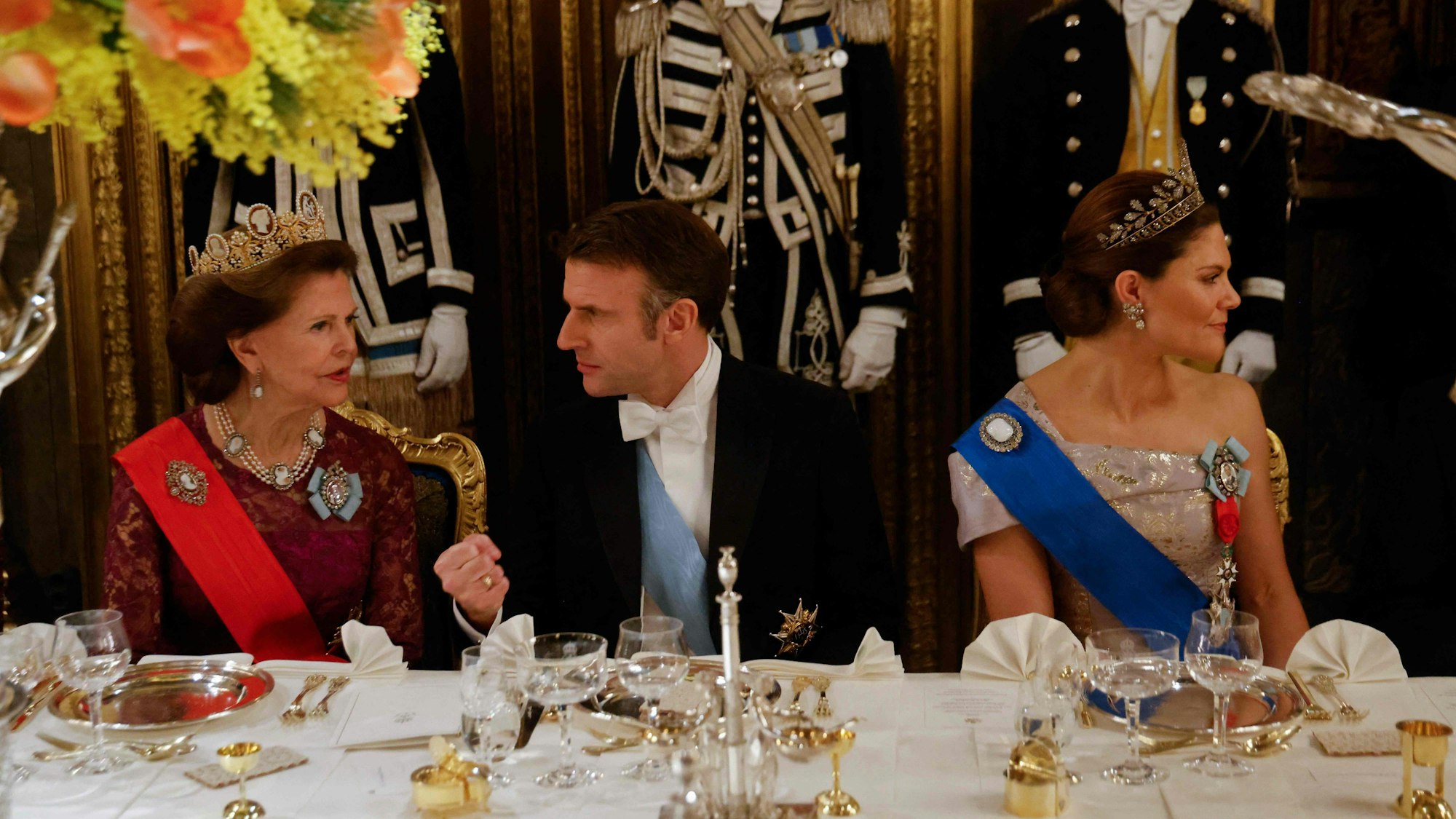 Präsident Emmanuel Macron (m) spricht mit Königin Silvia (l) neben Kronprinzessin Victoria (r) während eines Staatsdinners im Königlichen Palast in Stockholm.