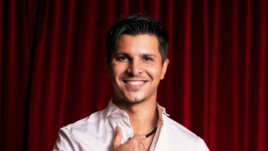 „Let's Dance“-Profitänzer Alexandru Ionel posiert im weißen Hemd vor einem roten Vorhang.&nbsp;