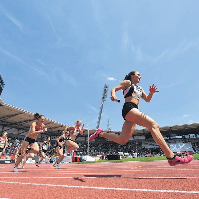 Frauen sprinten auf einer Tartanbahn in einem Stadion.