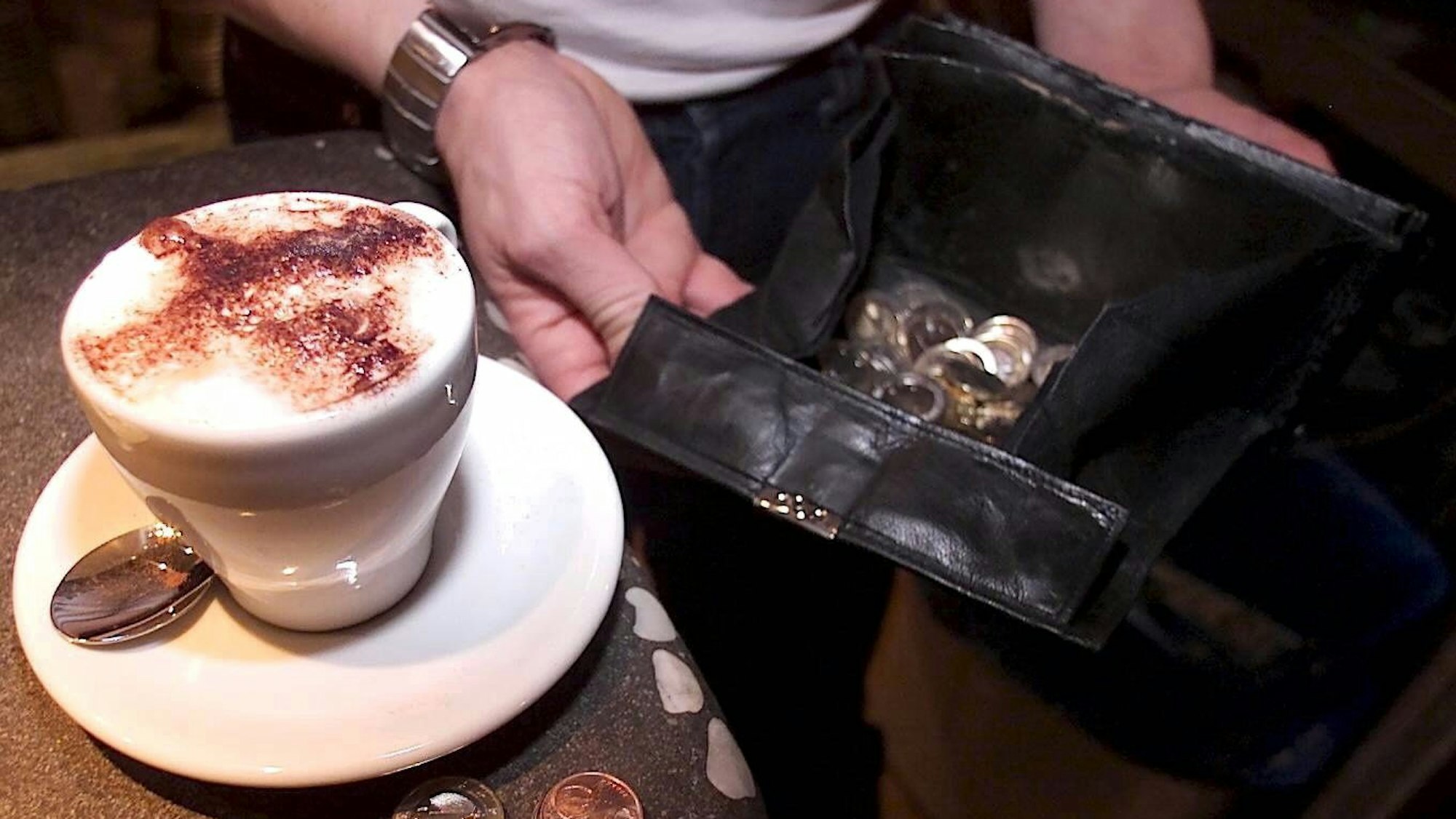 Ein Kellner hält seine Geldbörse auf, um einen bestellten Cappuccino abzukassieren.