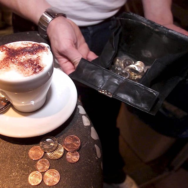 Ein Kellner hält seine Geldbörse auf, um einen bestellten Cappuccino abzukassieren.
