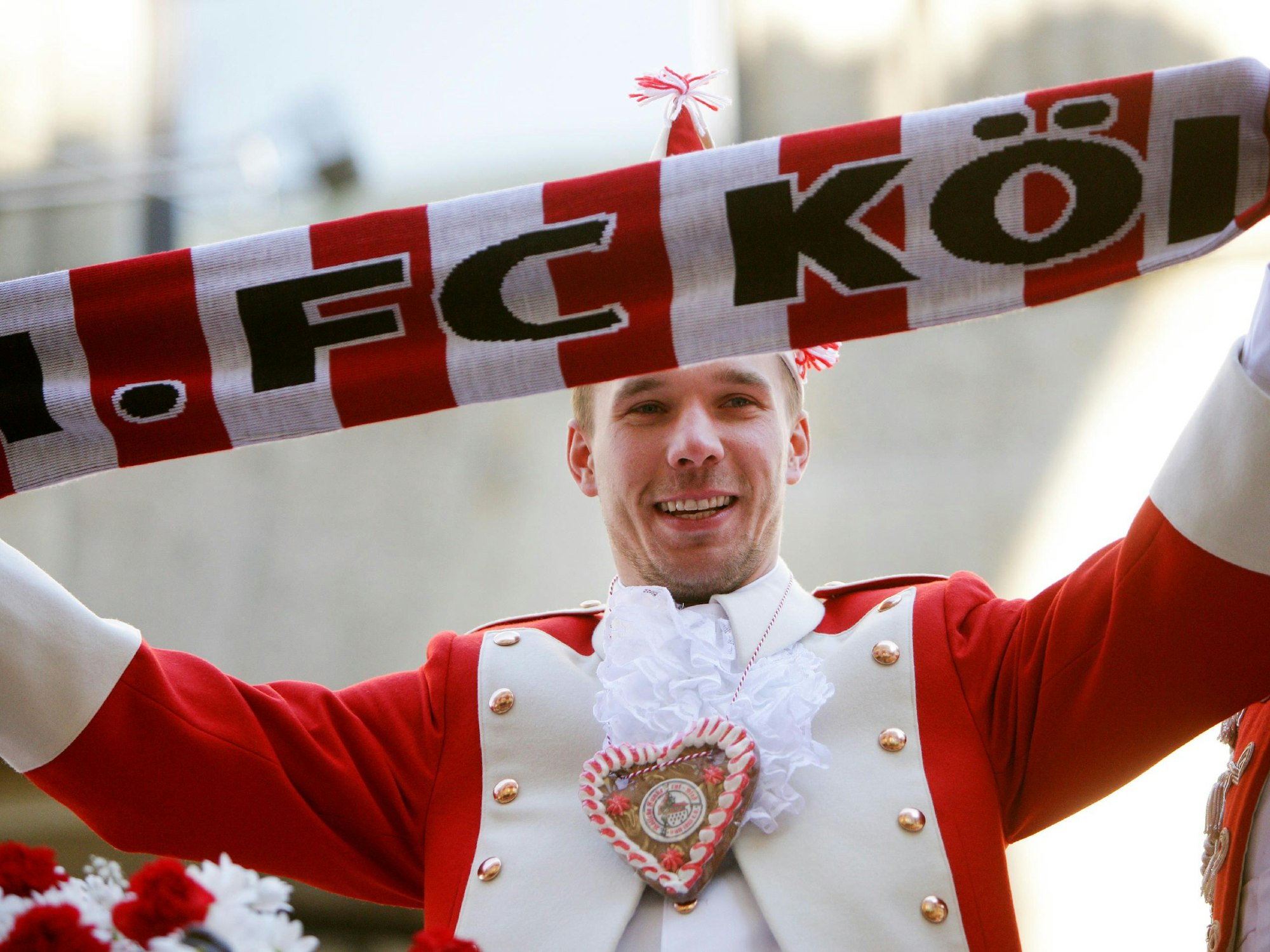 Lukas Podolski hält einen Schal des 1. FC Köln vor sich.
