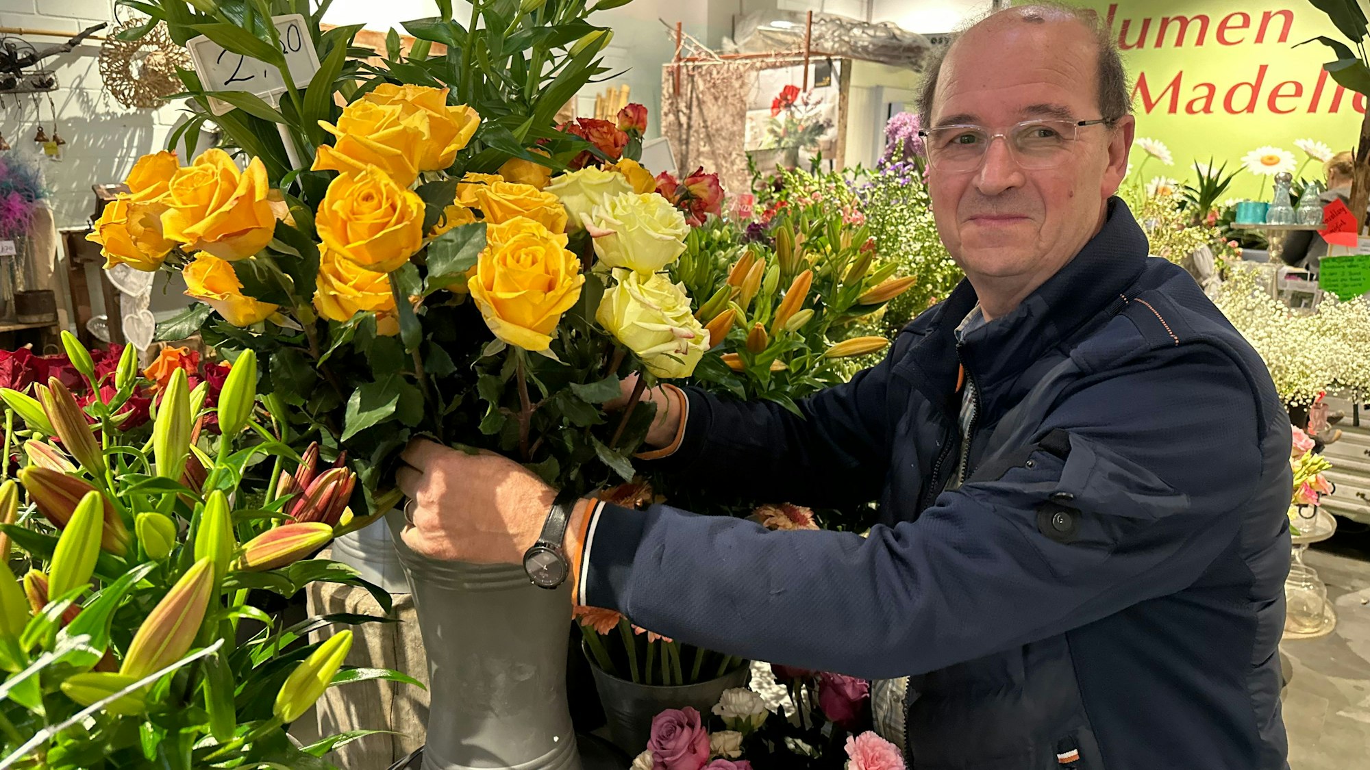 Blumenhändler Cornelius Geerlings mit gelben Rosen inmitten der bunten Blumen in seinem Laden.