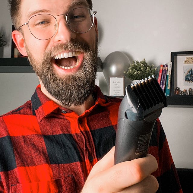 Lachender junger Mann mit Bart, Brille und Rasierer in der Hand
