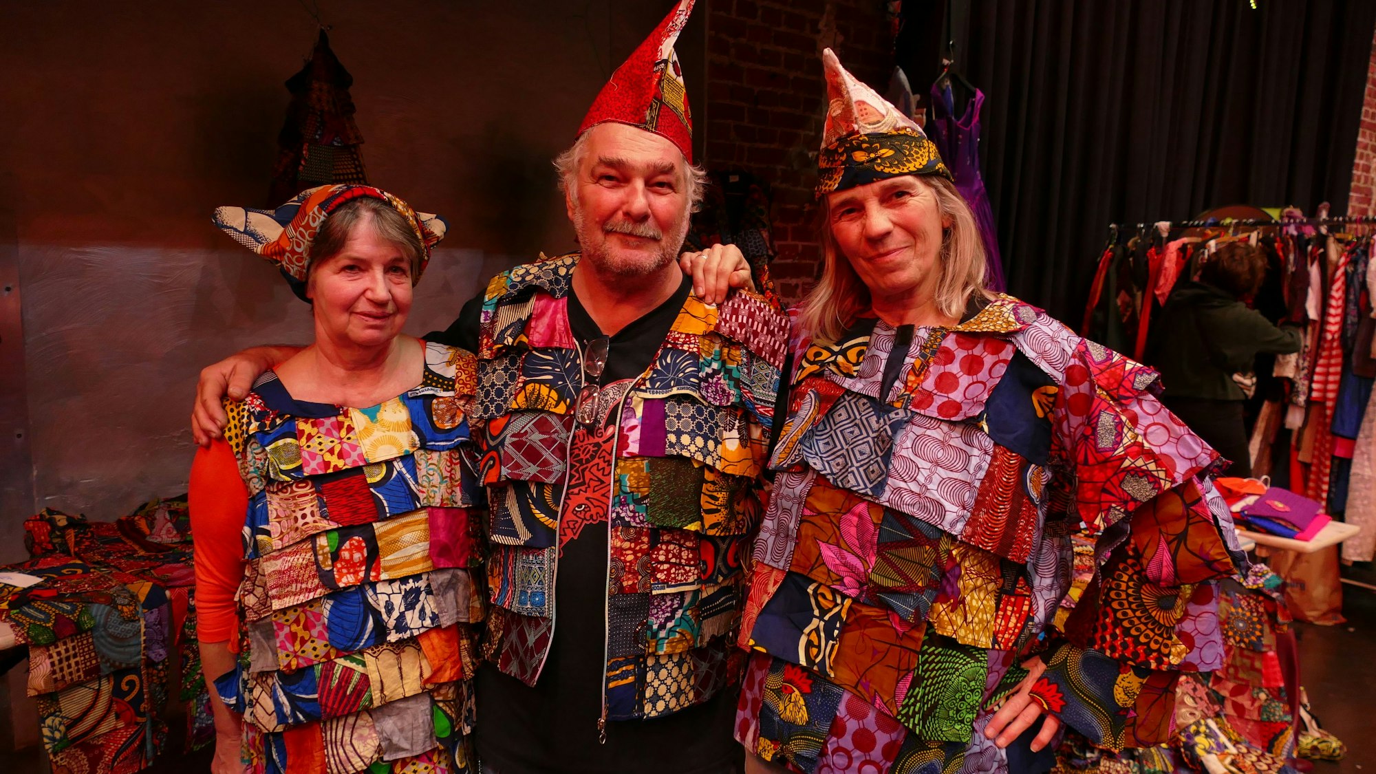 Zwei Frauen und ein Mann stehen nebeneinander in bunten Lappenclown-Kostümen.