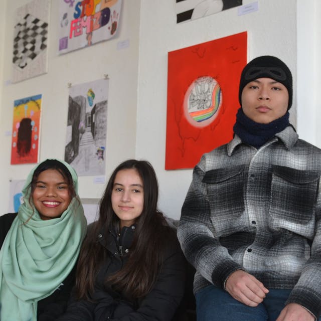 Schülerinnen und Schüler der Klasse EF der Gesamtschule Euskirchen sitzen vor ihren Bildern zum Thema „Gesicht zeigen“ in der Galerie FzKKE.