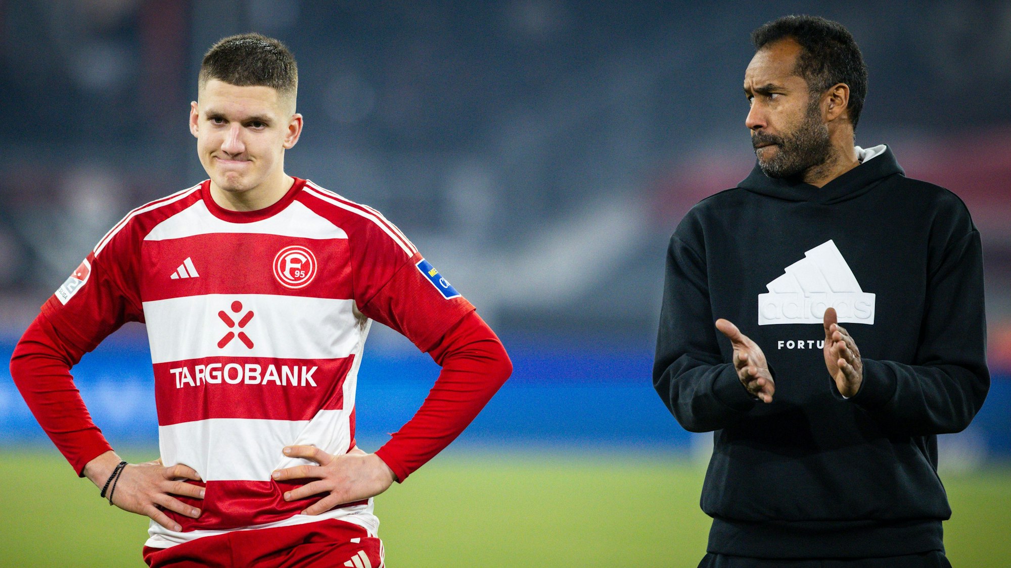 Fortuna Düsseldorfs Cheftrainer Daniel Thioune steht nach dem Schlusspfiff mit seinem Spieler Christos Tzolis vor der Fankurve.
