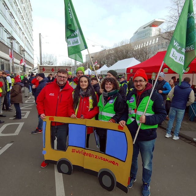 Zu sehen sind Streikende der KVB und der Umweltgruppe „Fridays for Future“ mit einem Plakat aus Pappe, das einen Bus darstellt. Er trägt die Aufschrift „#Wir fahrenzusammen“.&nbsp;