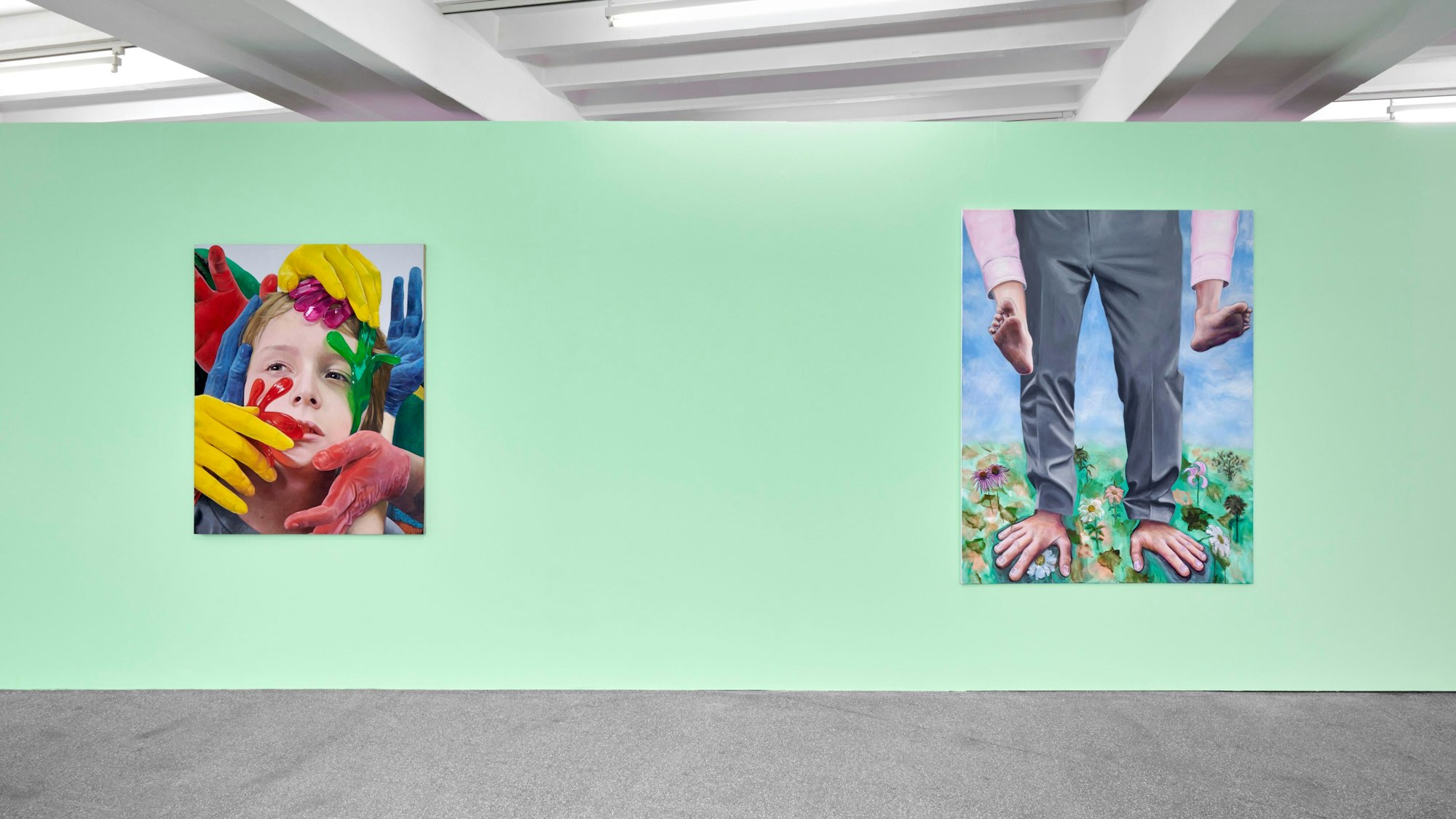 Zwei Bilder hängen an einer grünen Wand. Auf einem sind bei einem Mann Füße und Hände vertauscht.
