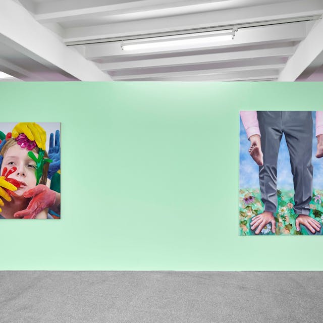 Zwei Bilder hängen an einer grünen Wand. Auf einem sind bei einem Mann Füße und Hände vertauscht.&nbsp;