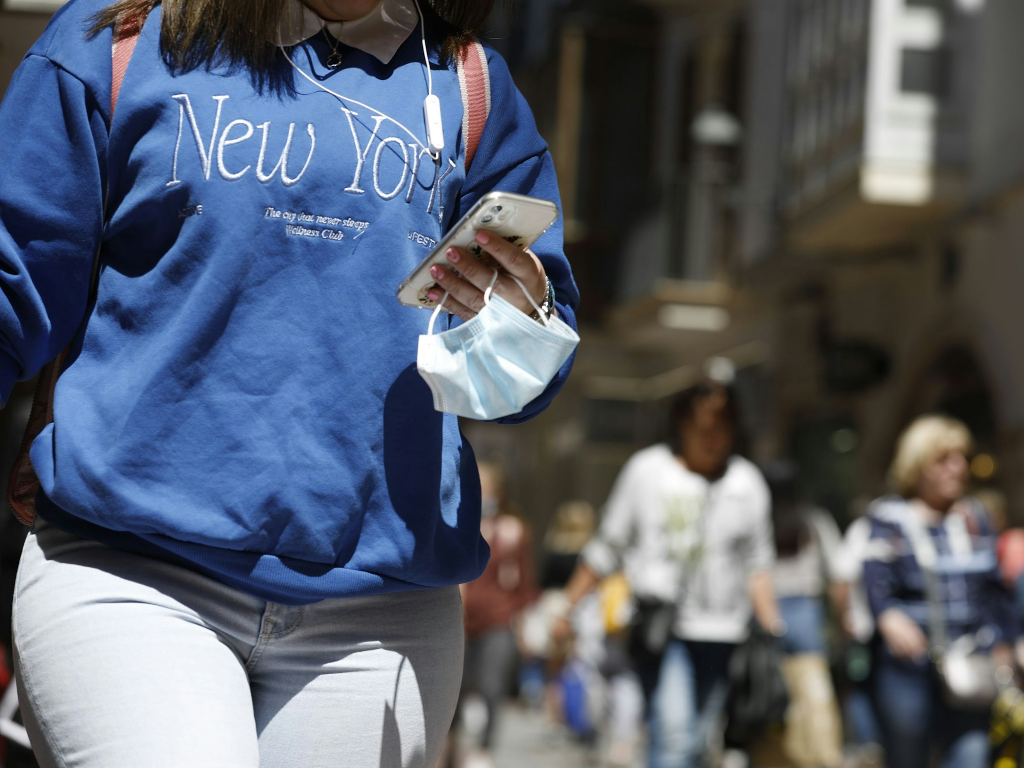 Eine Frau trägt ihre medizinische Maske am Handgelenk, während sie in der Innenstadt von Palma de Mallorca spazieren geht.