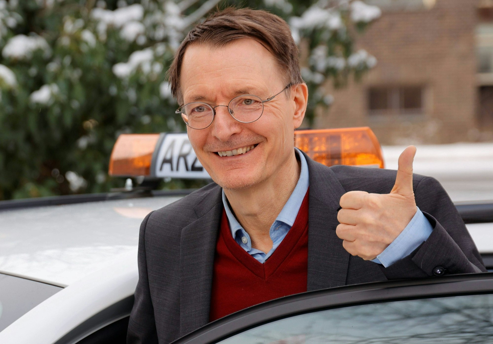 Bundesgesundheitsminister Prof. Karl Lauterbach steigt aus einem Auto und lacht in die Kamera.