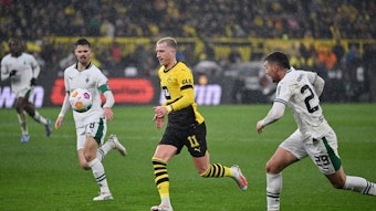 Ein Spieler von Borussia Dortmund setzt sich gegen zwei Spieler von Borussia Mönchengladbach durch.