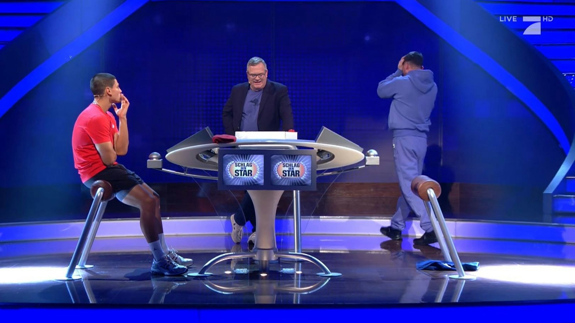 Musik-Star Bausa (r.) ärgert sich über seine Fehler im „Schlag den Star“-Duell mit Emilio Sakraya (l.). In der Mitte steht Moderator Elton.
