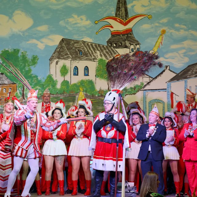 Prinz Hubertus Bollig, Bauer Paul Esser und Jungfrau Tobias Kohlenbaum stehen mit weiteren Karnevalisten vor dem Bühnenbild.