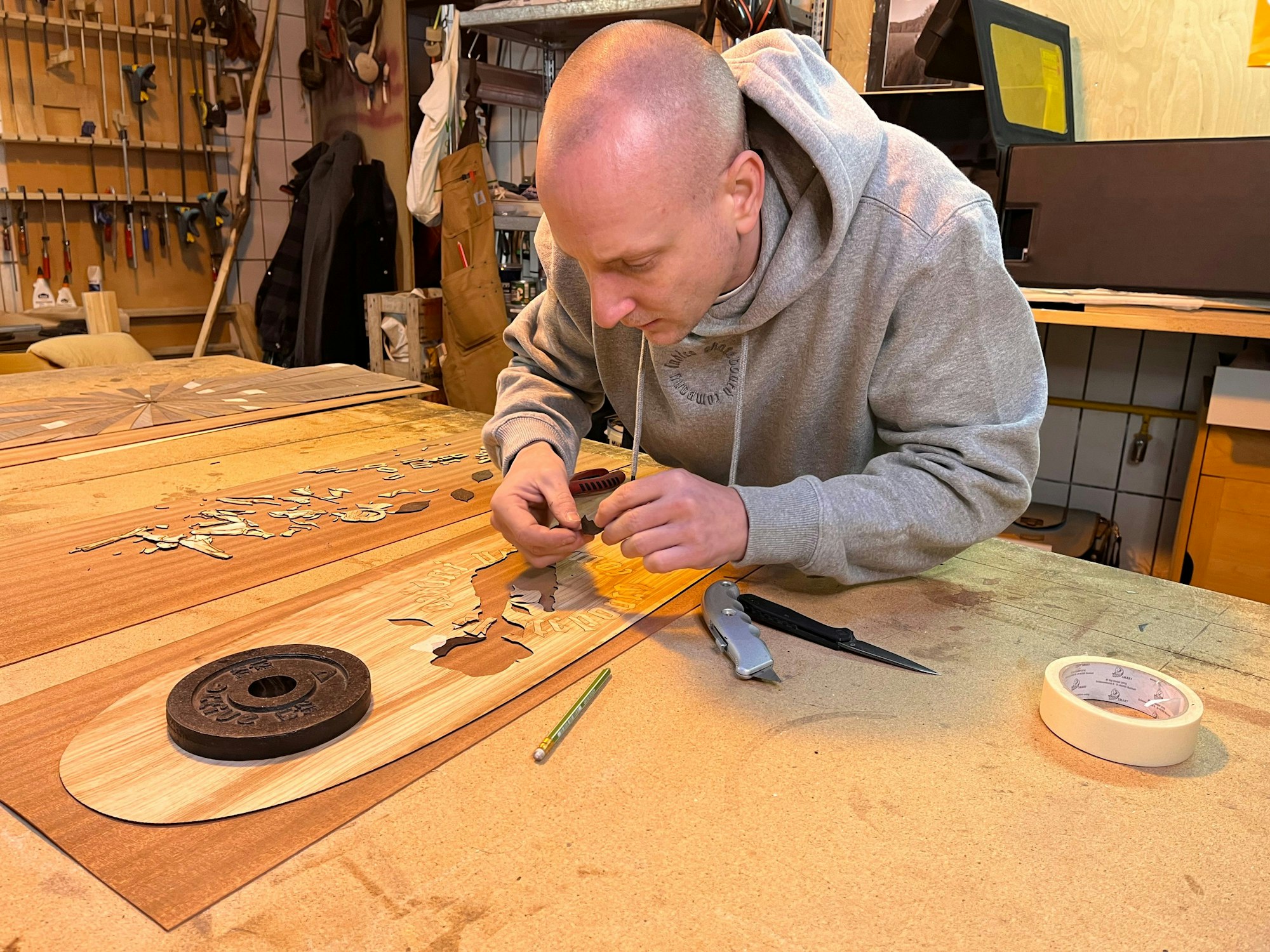 Ein Mann in einer Werkstatt arbeitet an einem länglichen Stück Holz.